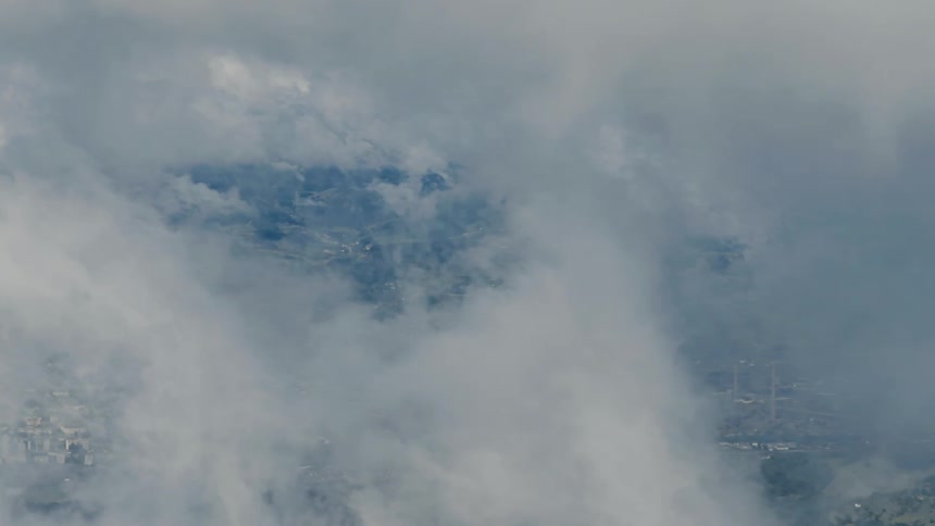 A serene aerial view shows a city and its surroundings through a hole in the clouds, gradually getting smaller