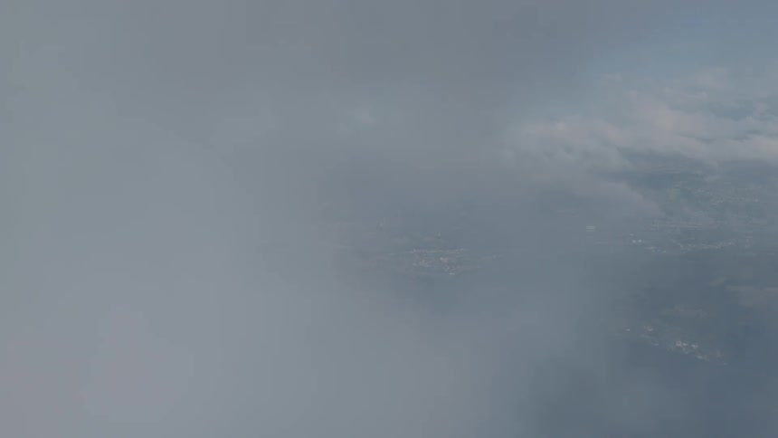 An aerial shot flying backward through the clouds, revealing a vast cityscape nestled within a lush green mountain valley
