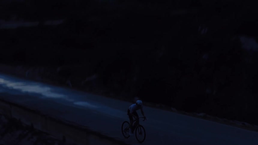 High-angle drone shot follows a determined cyclist training on a dark, empty road at dusk
