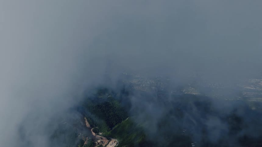 Immersive aerial view flying backwards through thick clouds to reveal a stunning city nestled among green hills