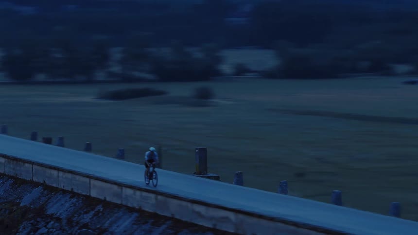 Aerial view of a cyclist riding on a scenic road alongside a tranquil lake during the blue hour