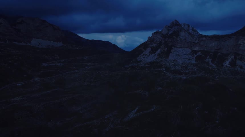 A dramatic aerial view pushing through a dark mountain valley under a moody, deep blue night sky