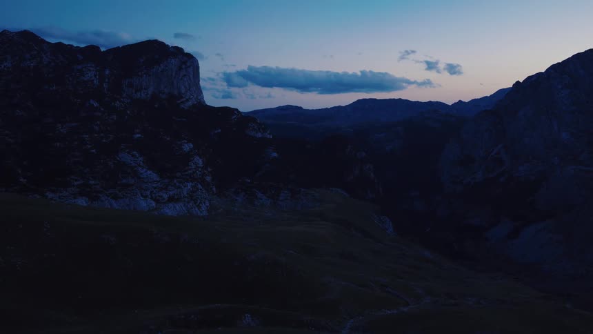 A tranquil drone shot slowly pulls back over a dark mountain valley during the serene blue hour of twilight