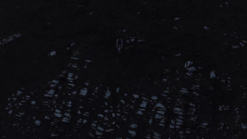 A cinematic top-down aerial shot reveals a lone wolf walking slowly across a dark, rocky, and barren landscape
