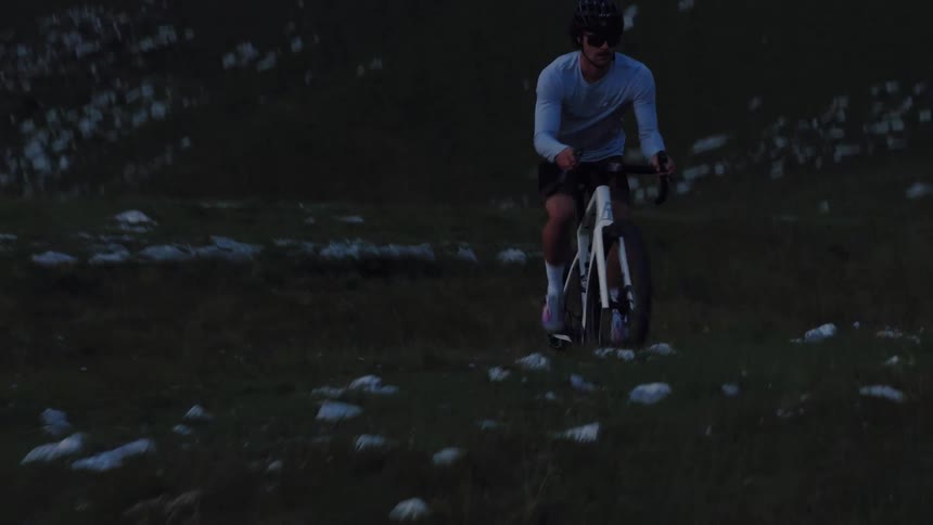 High-angle shot of a determined male cyclist in a helmet and sunglasses riding his bicycle up a steep, grassy mountain at dusk