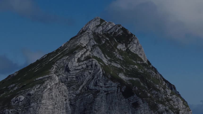 A dramatic time-lapse of clouds moving over a majestic, grass-covered mountain peak against a blue sky