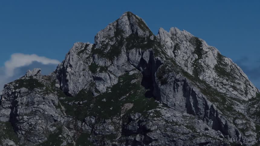 Slow zoom out from a rugged, sunlit mountaintop with a brilliant blue sky