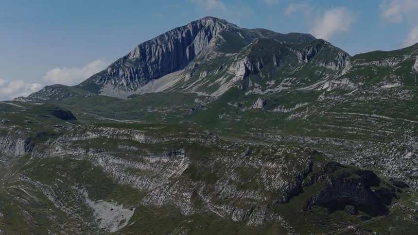 Stunning aerial shot slowly pulls back to reveal a majestic mountain peak and the rugged, green landscape below