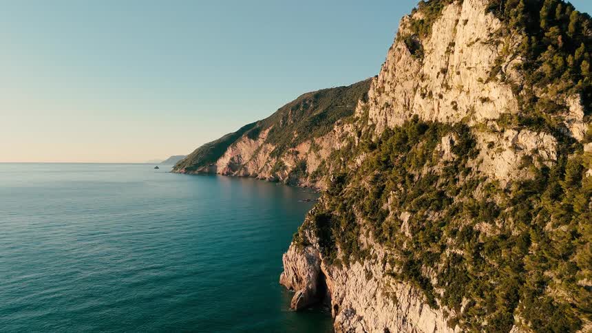 An aerial view of a majestic, sun-kissed cliffside coastline meeting the calm blue sea during a golden hour sunrise