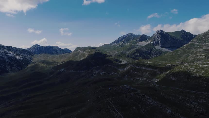 A majestic aerial view of a vast, rugged mountain range with deep shadows under a blue sky