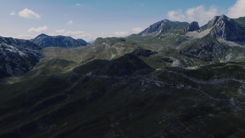 A slow aerial push-in shot reveals the vast, rugged landscape of a mountain range with a winding road
