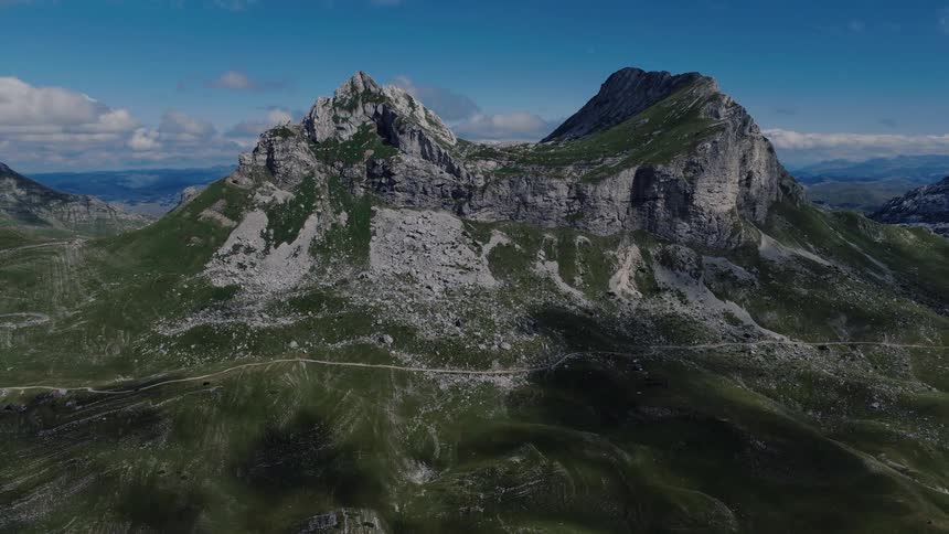 A majestic aerial view slowly pulls back from the stunning green and rocky mountain peaks of Durmitor National Park in Montenegro