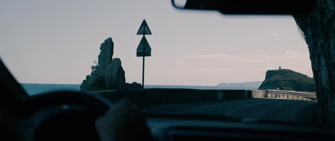 A scenic drive from inside a car along a winding coastal highway carved into rocky cliffs with a beautiful ocean view