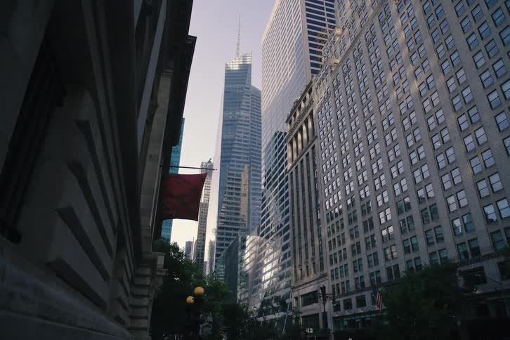 A slow pull-back shot from a low angle reveals the towering skyscrapers of New York City and a New York Public Library banner