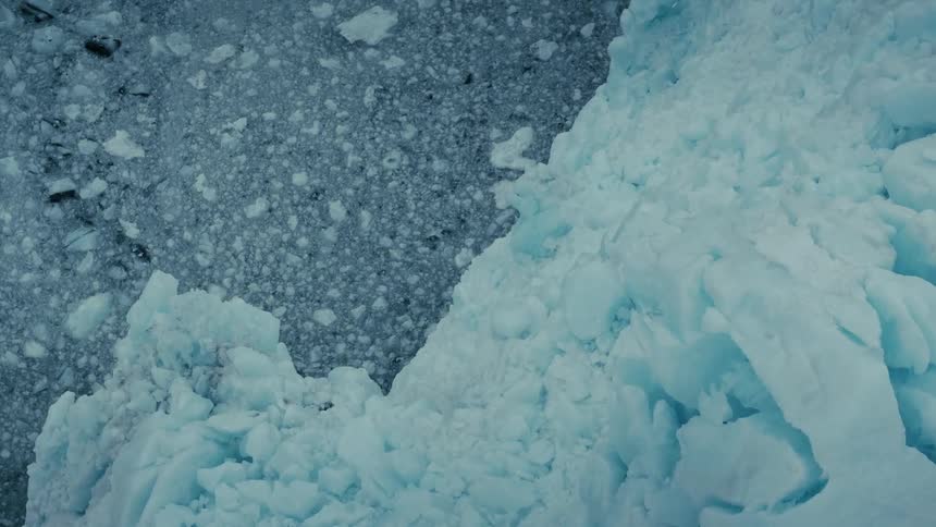 A stunning top-down aerial view of a massive glacier meeting the icy arctic water, filled with floating ice chunks