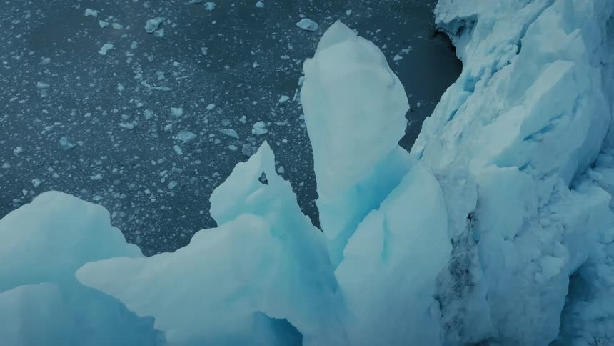 A high-angle view shows vast blue glacier ice formations in the cold, ice-filled Arctic water