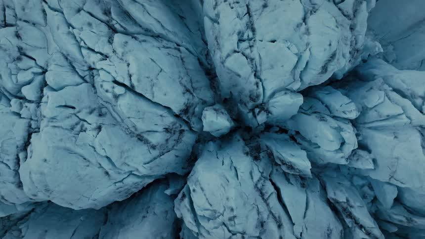 A stunning top-down aerial view reveals the intricate textures and deep blue crevasses of a massive, ancient glacier