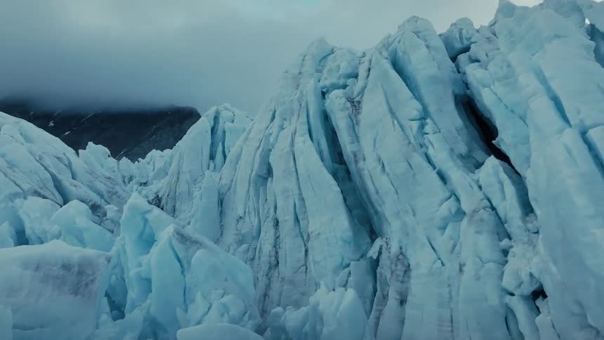 A close-up view of the jagged, blue ice formations of a massive glacier under a cloudy sky