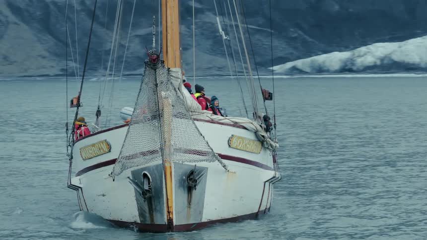 An old wooden sailboat with tourists aboard navigates a majestic arctic fjord with a massive glacier in the background