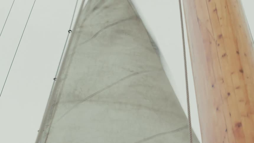 A close-up, low-angle shot of a sailboat's sail billowing in the wind against an overcast sky