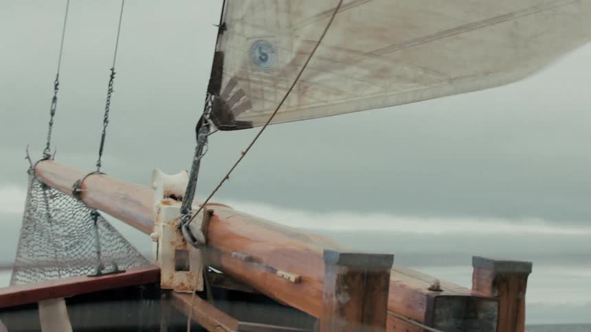 The bowsprit of a traditional wooden sailing ship plunges through rough seas on an overcast day