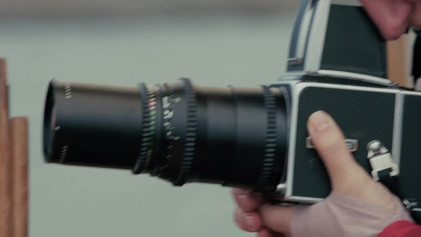 A photographer wearing a yellow beanie looks through the viewfinder of a vintage film camera with a large telephoto lens