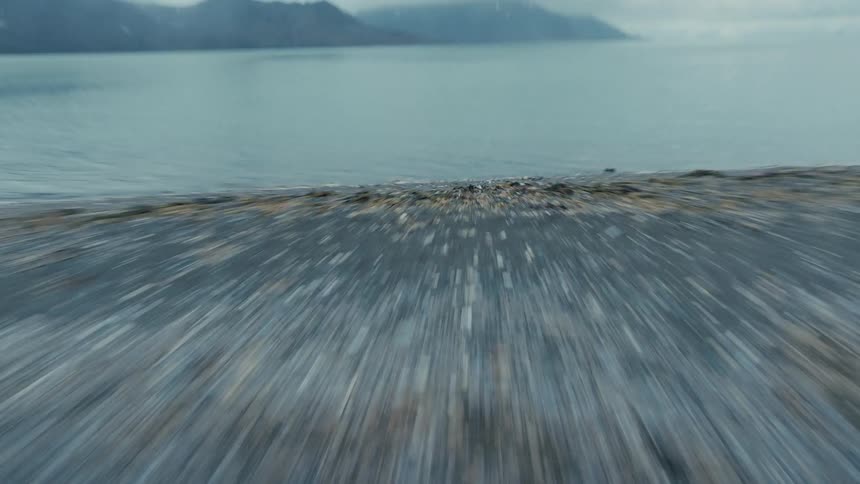 A fast-paced, low-angle shot speeds over a rocky beach and dives into the cold arctic ocean