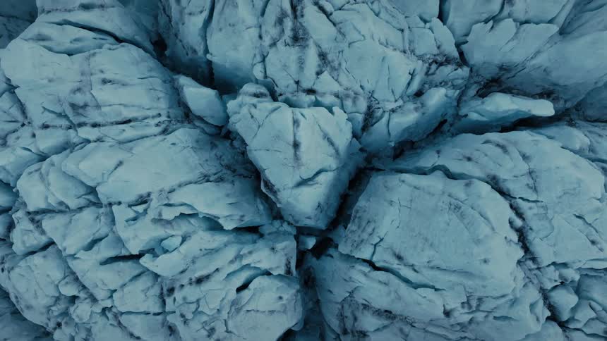 A stunning top-down aerial view slowly zooms out from the cracked, blue surface of a vast glacier