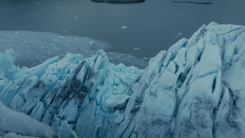 An aerial flyover captures the majestic and rugged beauty of a glacier's edge as it calves into the sea