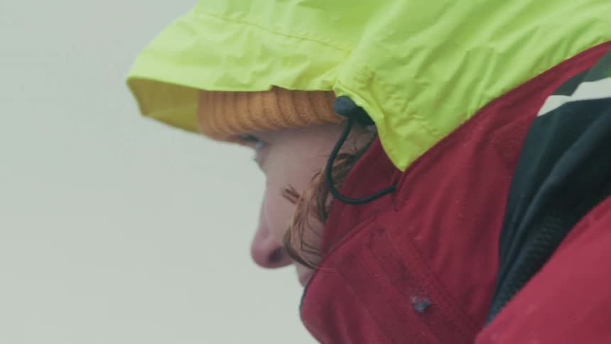 A close-up side profile of a person bundled in a colorful winter jacket and beanie, persevering through a harsh snowstorm