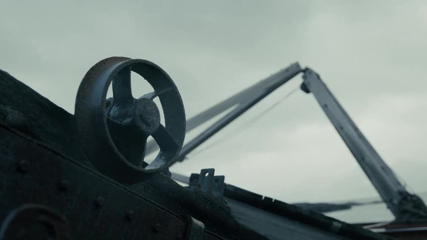 A static, close-up shot of a rusted, industrial wheel that's part of an old machine in a forgotten shipyard