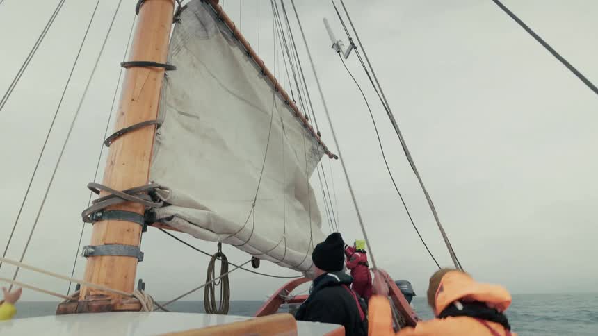 A sailing crew works together to handle the sails on a wooden boat during an ocean expedition