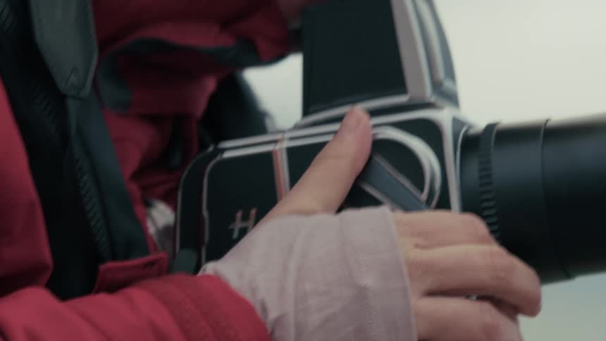 A photographer's hands adjust the focus and wind the film on a vintage medium format camera in slow motion