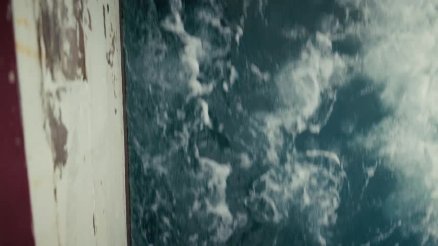 A vertical overhead shot of the turbulent, foamy ocean wake created by a moving boat