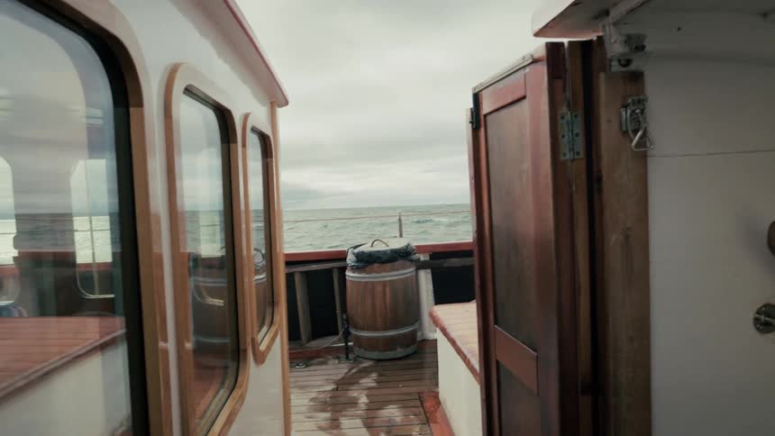 View from the wet, rocking deck of a wooden boat sailing on the ocean on a cloudy day