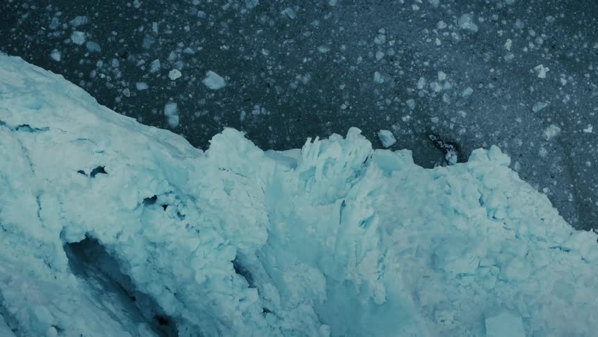 An aerial view captures the slow drift of ice fragments away from the edge of a vast, frozen glacier in a cinemagraph