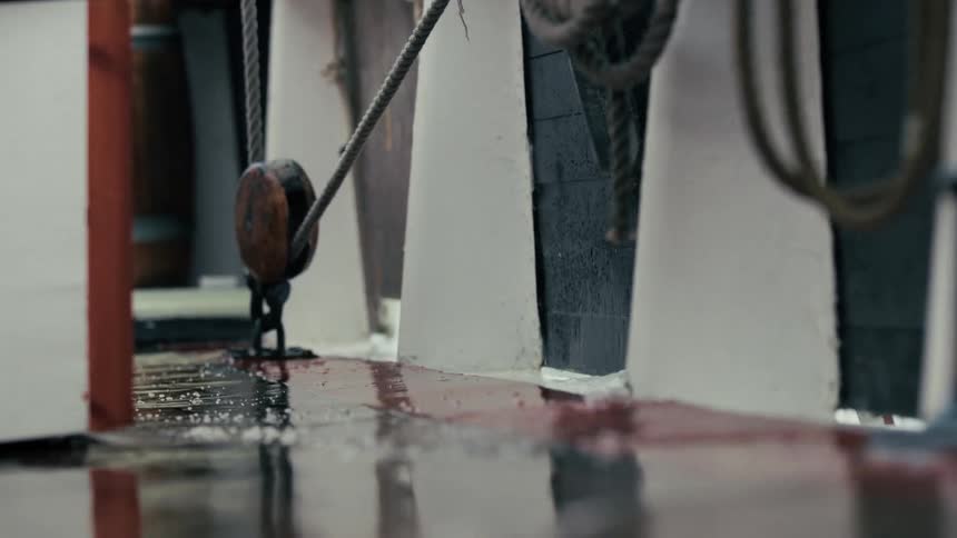 Slow motion close-up of blood being washed off the wet wooden deck of a ship at sea