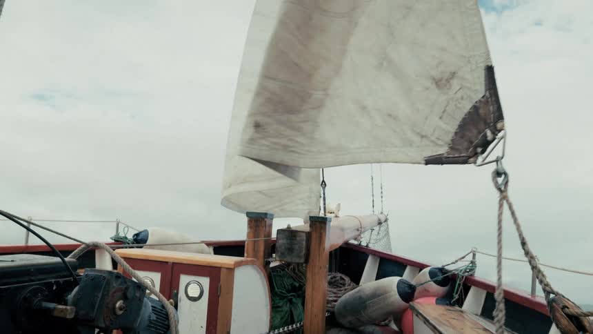 A view from the deck of a traditional wooden sailing boat as its sail catches the wind on a cloudy day