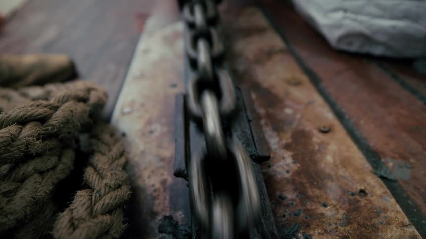 A close-up of a rusty anchor chain moving quickly through a winch on the wooden deck of a ship