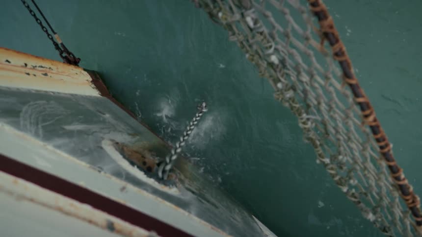 A muddy anchor is dropped from the side of a fishing boat into the ocean