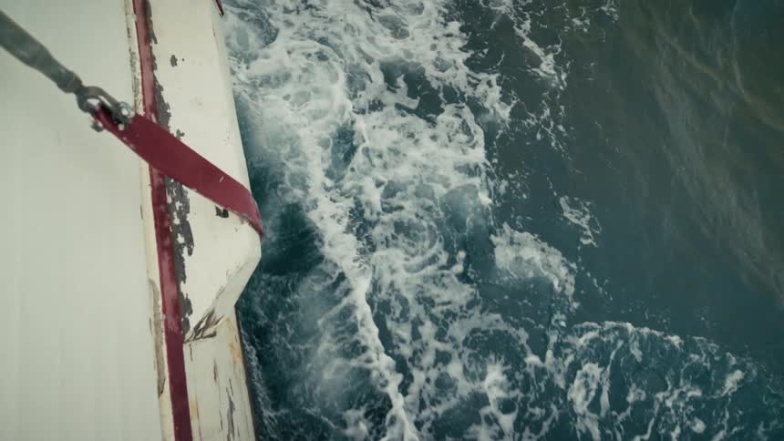 Slow motion top-down shot of the white wake created by a boat as it travels through the deep blue ocean