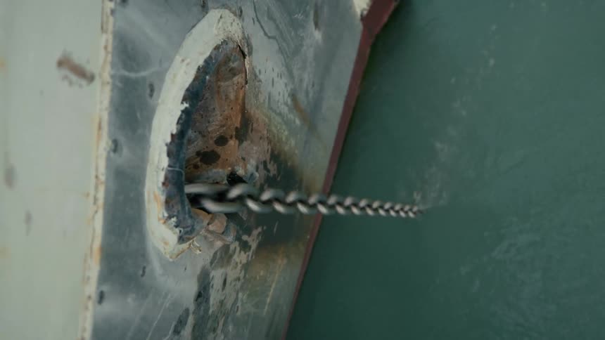A vertical view of a heavy anchor chain being pulled taut from the rusty hull of a ship into the water