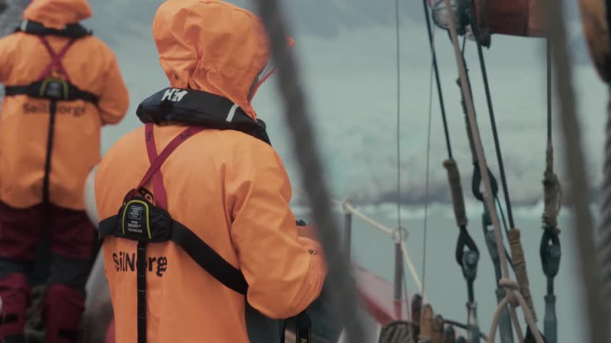 A photographer wearing a bright orange hooded rain jacket observes an icy glacier from the deck of a moving boat