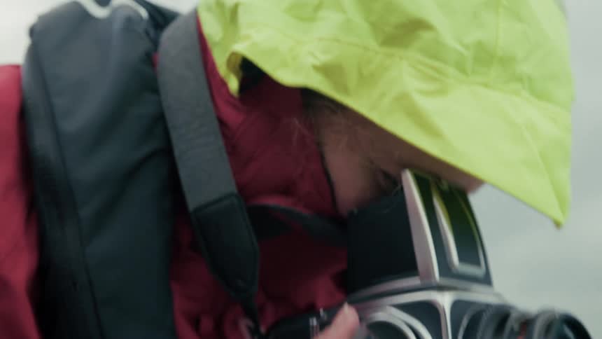 A photographer wearing a bright yellow hood adjusts the focus on a vintage Hasselblad camera while on a boat at sea