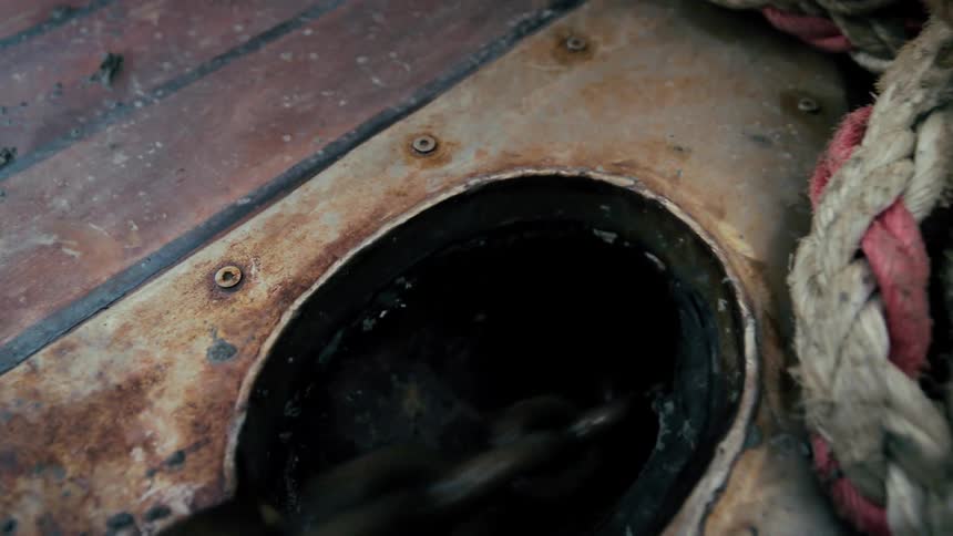 A heavy anchor chain rapidly descends into the hull of a rusty, weathered boat