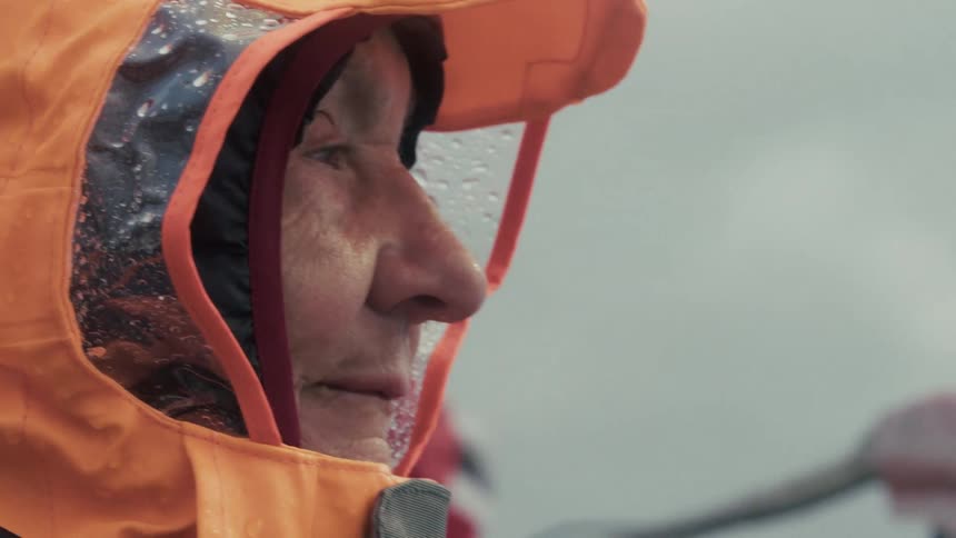 Slow motion close-up of a determined elderly woman in a hooded raincoat with a Norwegian flag waving in the rain