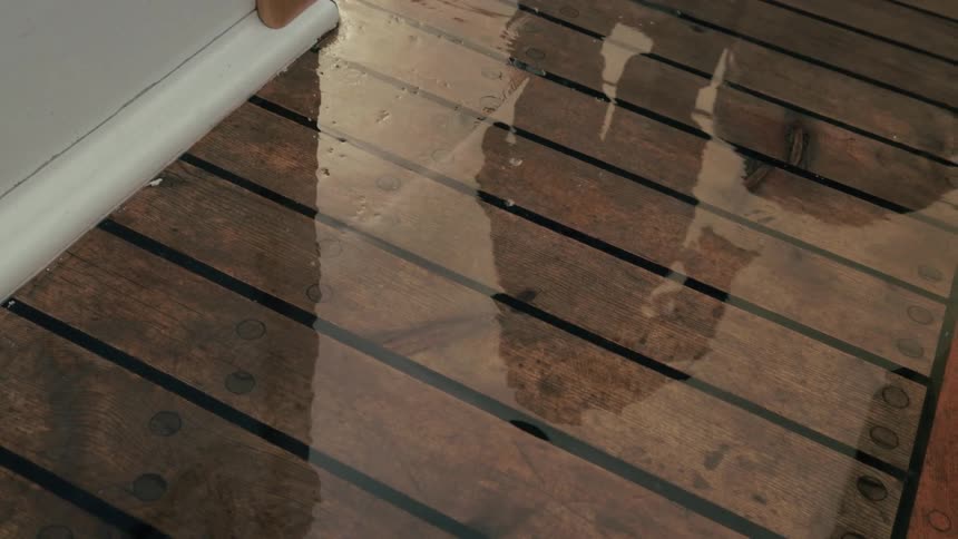 The abstract reflection of a person moves across the wet wooden deck of a boat