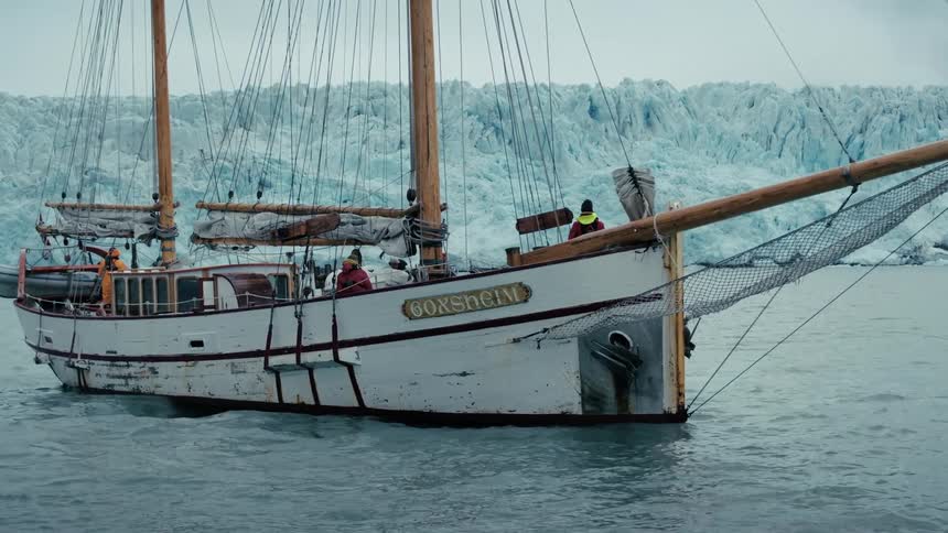 A majestic wooden sailboat navigates the icy waters in front of a colossal glacier in the Arctic