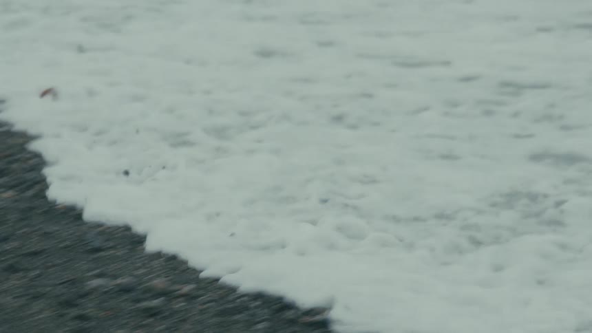 Foamy ocean wave recedes in slow motion over a rocky shoreline