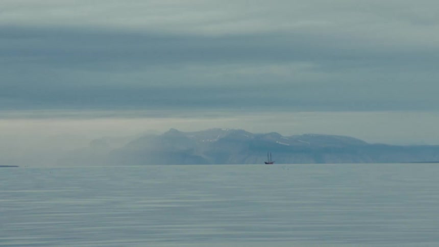 A solitary schooner sails on a calm, misty sea with distant snow-capped mountains on the horizon